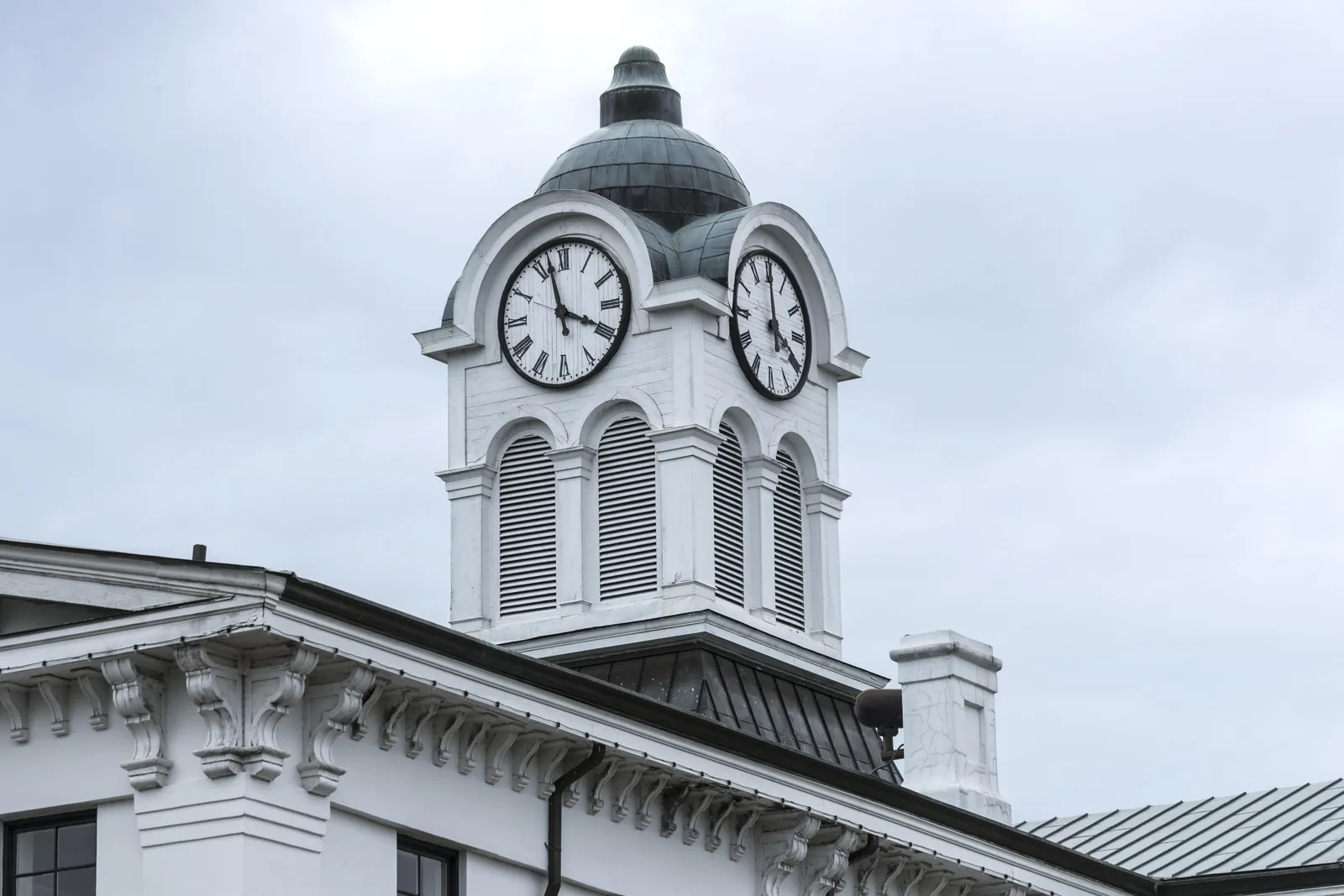 The white clock tower and copper dome of the Lafayette County Courthouse in Oxford, Mississippi, above the bracketed cornice of the building, against an overcast sky